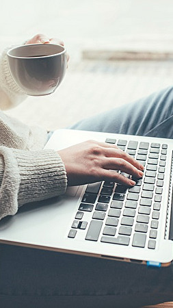 Frau sitzt mit Laptop im Schoß und Teetasse in der Hand