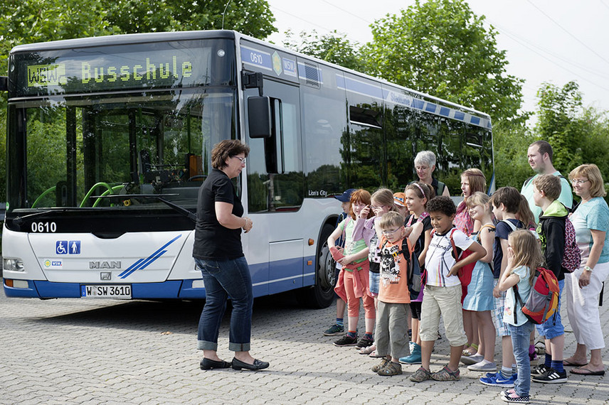 Eine Frau begrüßt Kinder vor dem Bus.