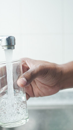 Jemand füllt ein Glas mit Wasser am Wasserhahn
